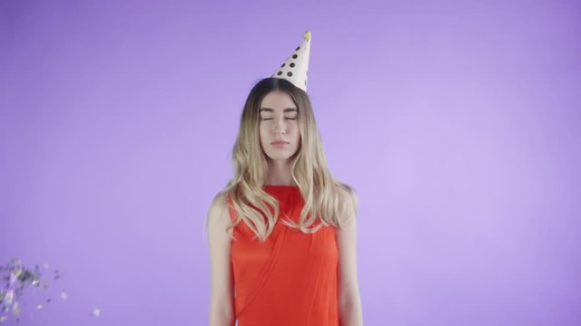Beautiful girl in party hat are standing under confetti on a purple background.