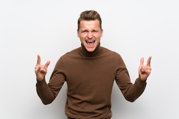 Blonde man over isolated white wall making rock gesture
