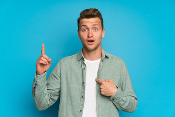 Blonde handsome man with green shirt with surprise facial expression