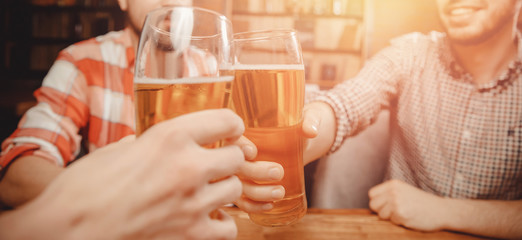 Glasses and bottle of dark beer, friends clink in bar wooden table. Banner
