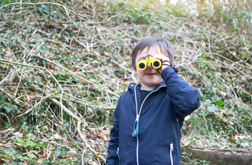 Active kid boy in the forest looking through binoculars. child exploring nature with binoculars at the mountain, Travel and adventure concept