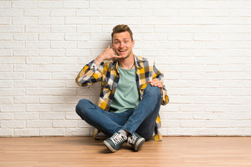 Blonde man sitting on the floor making phone gesture. Call me back sign