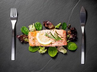 Grilled salmon fillet with salad on black slate plate