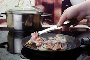 fry the bacon in the frying pan, the girl's hand puts bacon in the frying pan, cooking in the kitchen on the ceramic stove