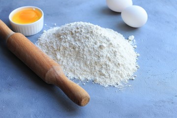 Preparation of dough, flour, eggs and rolling pin on gray background.