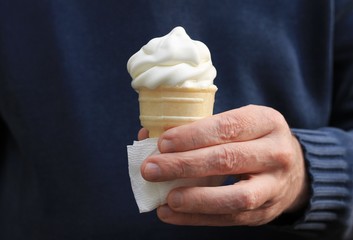 White ice cream cone melting in a man's hand, hand in a long sleeve sweater.