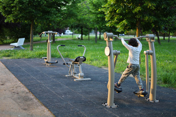 AREA SPORT CON ATTREZZI PER FARE GINNASTICA IN UN PARCO CITTADINO E BIMBO CHE PROVA UN ATTREZZO