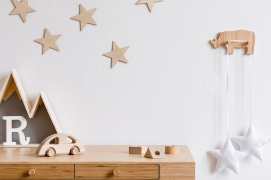 Stylish and cozy childroom with wooden accessories, toys, mountain box, car, basket and stars pattern on the background wall. Bright and sunny interior. Template, Copy space for inscription, products.