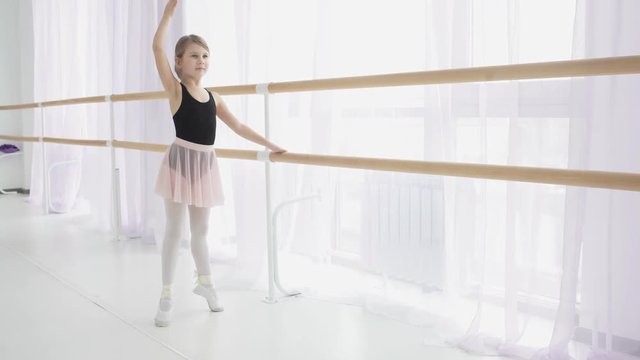Young ballerina doing exercises near ballet barre in the studio.