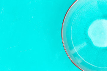 Half of empty turquoise bowl plate on turquoise table background with copy space