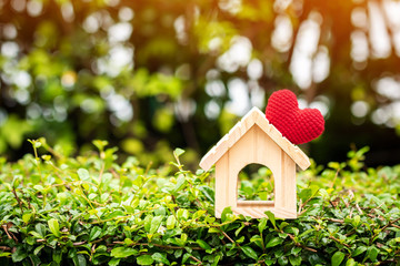 The buying a new real estate as a gift to family or the one loved concept, a home model tied with red heart put on the wood on sunlight in the public park.