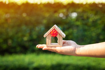 The buying a new real estate as a gift to family or the one loved concept, a man hand holding a home model tied with red ribbon in the public park.