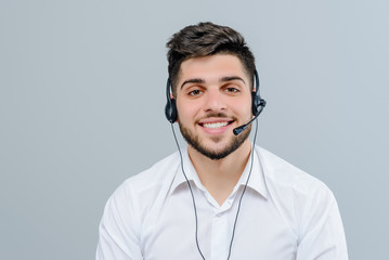 Handsome middle eastern man working with headset answering business calls as tech support dispatcher isolated over grey background