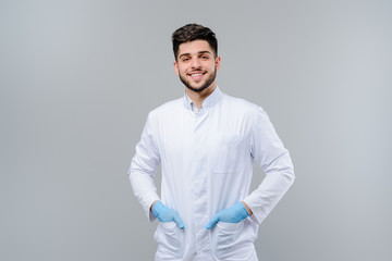 Handsome young medical doctor in gloves isolated over grey background