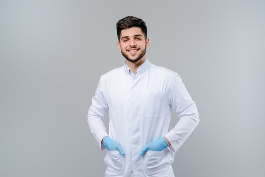 Handsome young medical doctor in gloves isolated over grey background