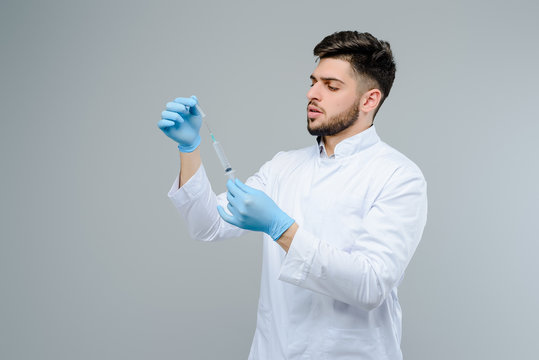 Male medical doctor in gloves filling the suringe isolated over grey background