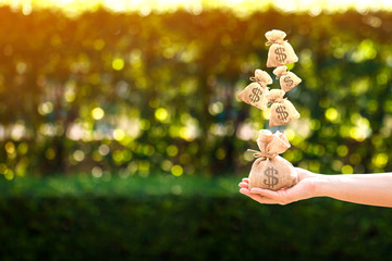 Women hands hold a money bags and dropping on the top in the public park for loans to planned...