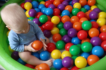 One year old baby boy is playing in ball pool on safety playground. Having fun with  toys