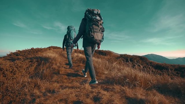 The hikers with camping backpacks walking to the mountain top. slow motion