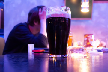 Glass with beer on the table in the bar. Against the background of a drunk man.