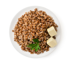 Boiled buckwheat in a plate with parsley leaf and butter on a white. The form of the top.