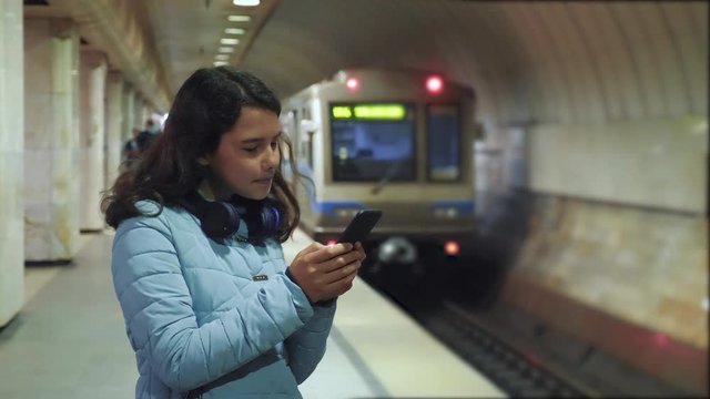 girl teen in the underground subway rides in the subway waiting for the arrival of train, holds smartphone. little girl brunette daughter search the internet on the web social networks lifestyle