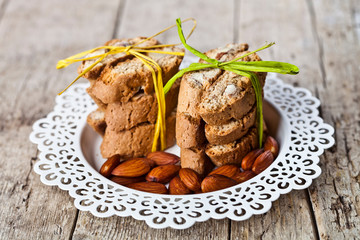 Almond seeds and fresh Italian cookies cantuccini stacked on white plate on ructic wooden table background.