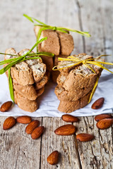 Fresh Italian cookies cantuccini stacks and organic almond seeds on white paper on ructic wooden table background.