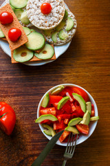 vegan rice bread with avocado and tomatoes on the white plate on wooden desk. Vegan breakfast rice tortillas with avocado and fresh salad with tomatoes and pepper. Rice cakes with sliced avocado.