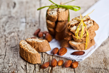 Homemade fresh Italian cookies cantuccini stacks and organic almond seeds on white paper on ructic wooden table background.
