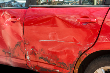 Damaged door of the red car. Closeup of hole accident in the side door of the red car. Red car dent in a door in the street after a broken accident.
