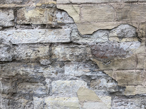 fallen plaster from a old yellow brick wall with lots of cracks.