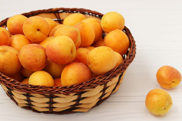 Ripe apricots are located in a wicker basket on a white background
