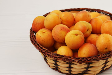 Ripe apricots are located in a wicker basket on a white background