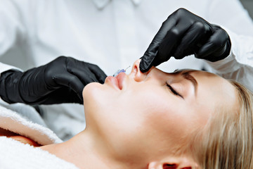 The doctor cosmetologist makes prick in the nose to correct the hump of a beautiful woman in a beauty salon.