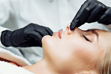 The doctor cosmetologist makes prick in the nose to correct the hump of a beautiful woman in a beauty salon. - 269743449