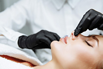 The doctor cosmetologist makes prick in the nose to correct the hump of a beautiful woman in a beauty salon. - 269743475