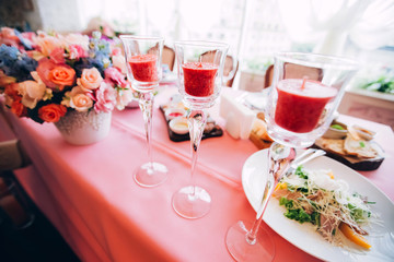 wedding decor in the style of boho. flower arrangements with roses, candles in glass candlesticks. table with pink tablecloth.
