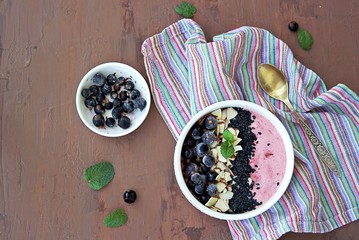 Smoothie bowl based on mashed berries, banana and natural yogurt in a white bowl. Decorated with frozen blackcurrant, sliced almonds and black sesame seeds. Healthy dessert. Top view, copy space.