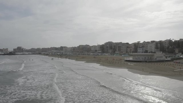 Aerial view of the coast of Anzio, a small sea town near Rome, in Italy. There is no one on the beach on this cold spring day. The blue sea with its waves is rough. In the sky there are some clouds.