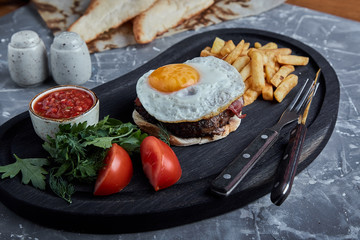 Beef steak with egg and salad from greens and vegetables. Gray background, table setting, fine dining