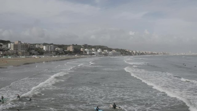 Aerial view of the coast of Anzio, a small sea town near Rome, in Italy. There is no one on the beach on this cold spring day. The blue sea with its waves is rough. In the sky there are some clouds.