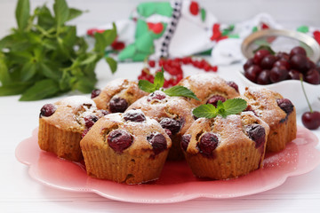 Cupcakes with cherries are located on a plate on a white background