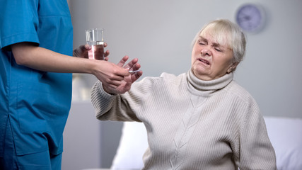 Capricious old woman rejecting medication from medical worker, treatment