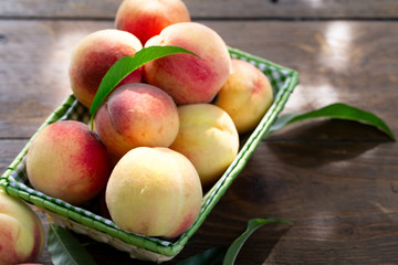 Fresh peaches fruits with leaves in basket on dark wooden rustic background