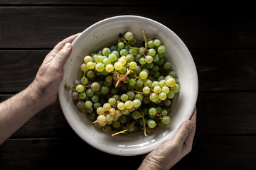 Male hands holding a bowl with white grapes on wooden table