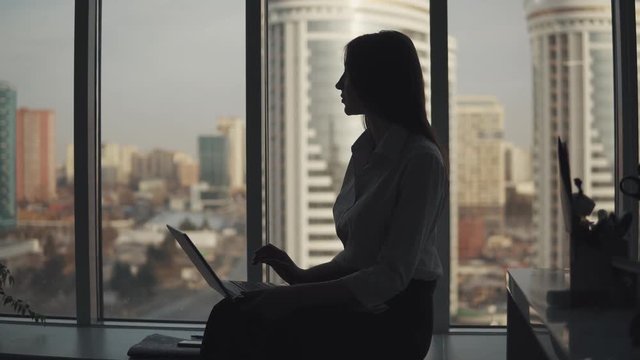 Silhouette of an attractive girl working on a laptop in an office near the window. business woman working alone
