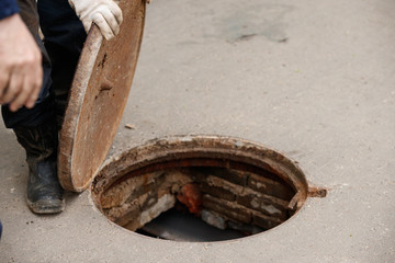 Dangerous open sewer manhole, a danger to people walking along the street within the city. Foreman closes the hatch cover. Repair of the pipeline under the ground.