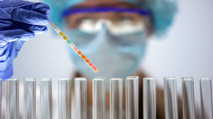 Scientist holding litmus paper analyzing reaction, chemical experiment, test