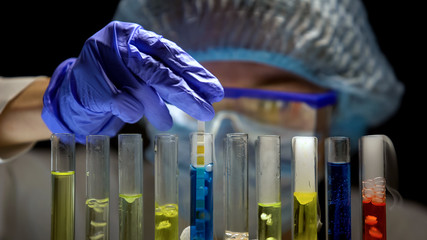 Scientist measuring acidity level in tube with blue liquid in dark laboratory